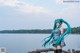 A woman with long blue hair standing on a log by the water.