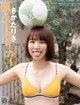 A woman in a yellow bikini holding a soccer ball on her head.