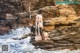 A woman sitting on a rock in the water holding a spear.