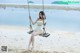 A woman sitting on a swing on a beach.